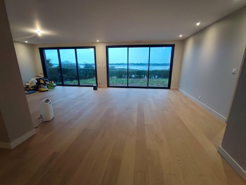 Parquet chêne clair dans un salon lumineux ouvert sur un étang : pose de parquet contrecollé en Bretagne sud.