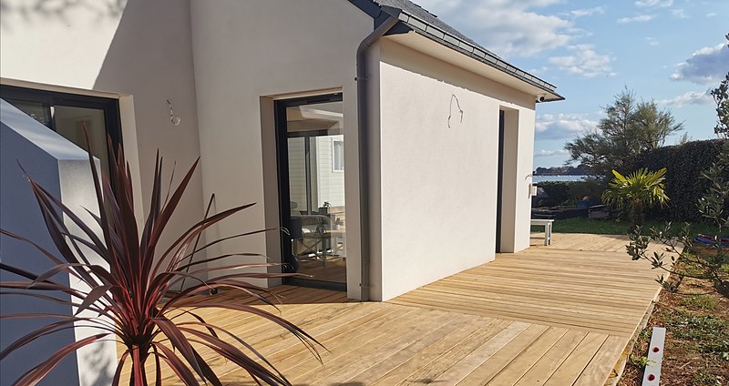 Vue d'ensemble d'une terrasse en chêne thermo depuis le bord de l'étang : aménagement extérieur bois en Bretagne.